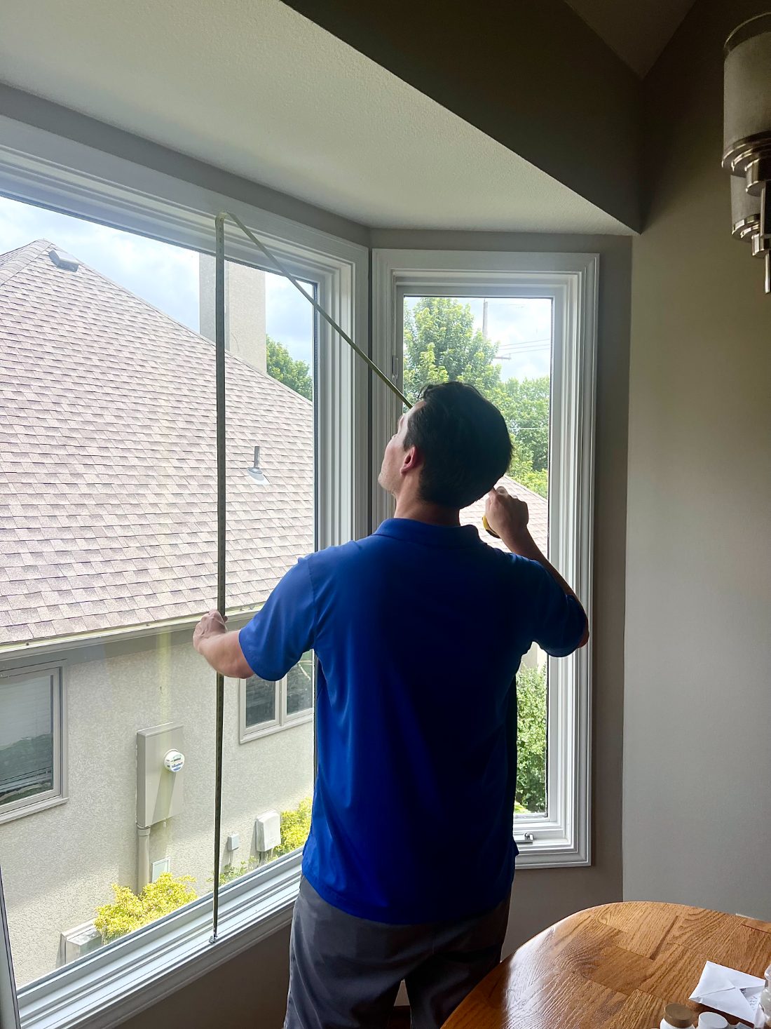 A One Stop Decorating designer measuring a bay window with a tape measure during an in-home visit in Kansas City