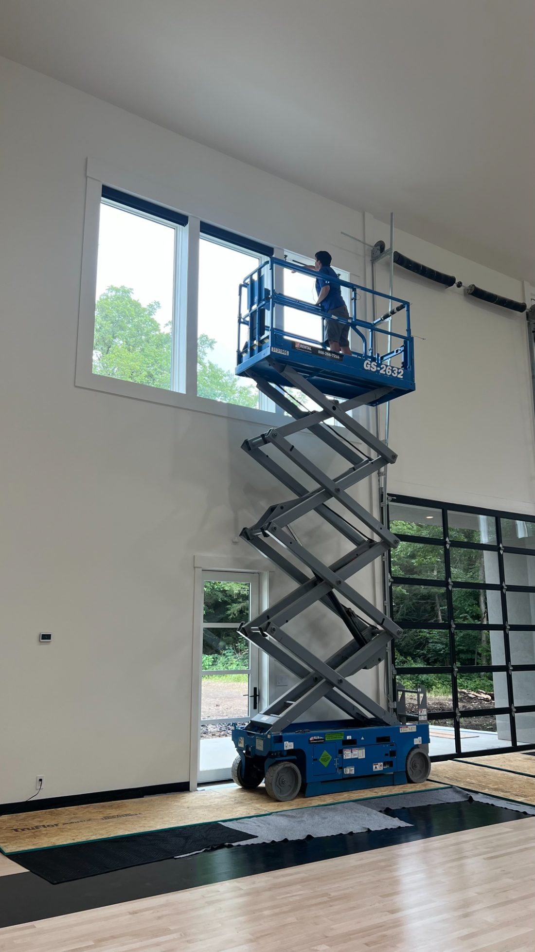 A One Stop Decorating installer on a scissor lift fitting custom shades on tall, two-story windows in a Kansas City home